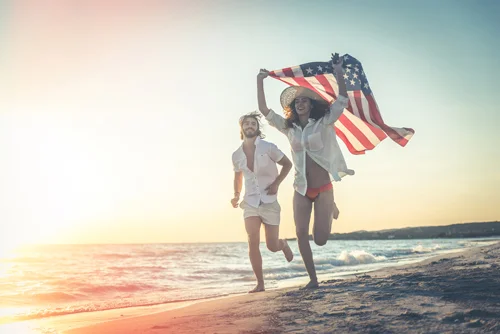 A couple with a U.S. flag running along the beach